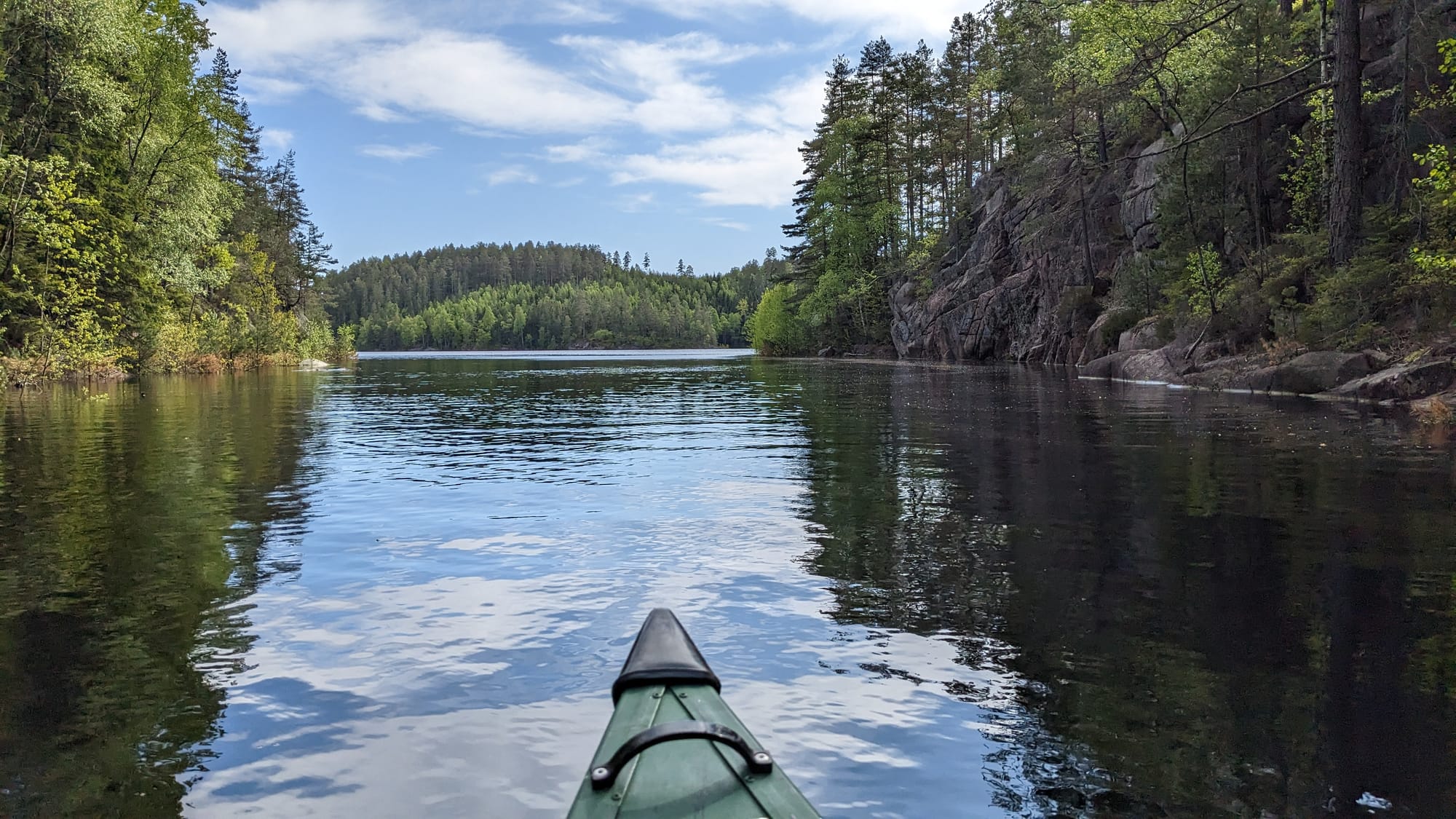 View from a canoe on a forest lake, surrounded by steep rock and spring foliage.