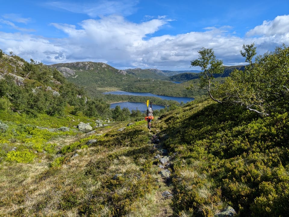 Hiker carrying a backpack with raft across open highlands in southern Norway.